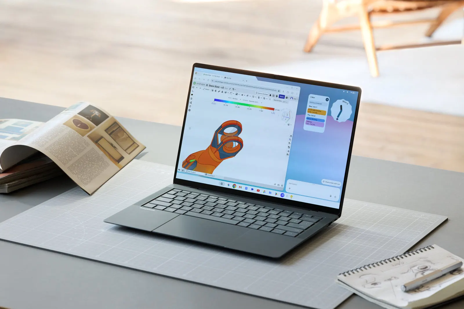 Otwarty laptop ASUS Googlebook 14 w ciemnoszarej obudowie stoi na biurku, na ekranie OLED widać okno programu CAD z pomarańczowym modelem 3D, obok widżety pulpitu, a na dole pasek ikon aplikacji.